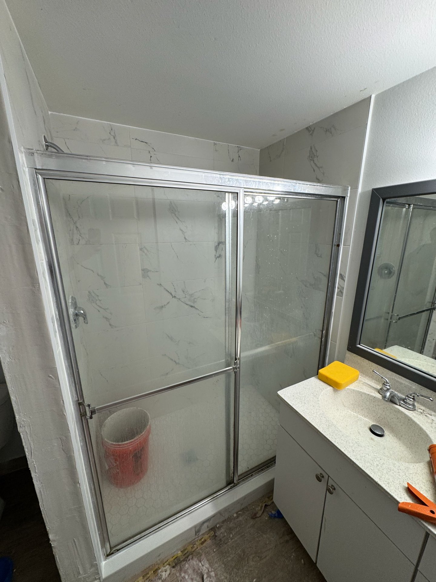 Finished marble-look porcelain shower with hex mosaic floor and sliding glass door in a Fort Lauderdale, FL apartment